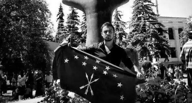 Нартан Кылыч держит черкесский флаг перед памятником жертвам Кавказской войны в Нальчике. Фото:  Аслан Щакуэ, Фатима Тлисова и Ольга Эфендиева-Бегрет https://www.facebook.com/photo.php?fbid=10153411014089002&set=a.10150641558564002.436428.531449001&type=1&fref=nf&pnref=story