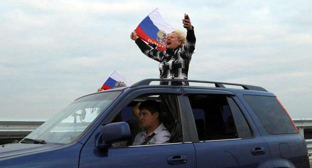 Женщина держит российский флаг , проезжая по мосту в Крым. Фото REUTERS/Pavel Rebrov Женщина держит российский флаг , проезжая по мосту в Крым. Фото REUTERS/Pavel Rebrov