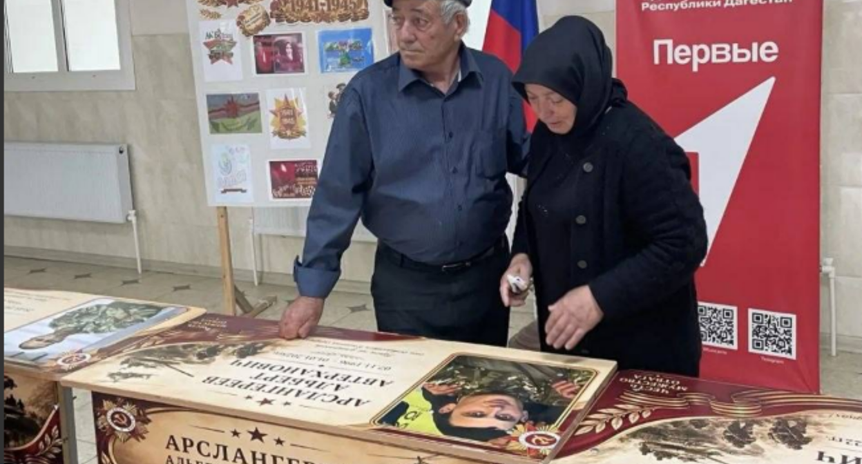 Родные на открытии именной парты. Скриншот фото администрации Бабаюртовского района от 25.05.26, https://t.me/babayurtrayon/12221?single