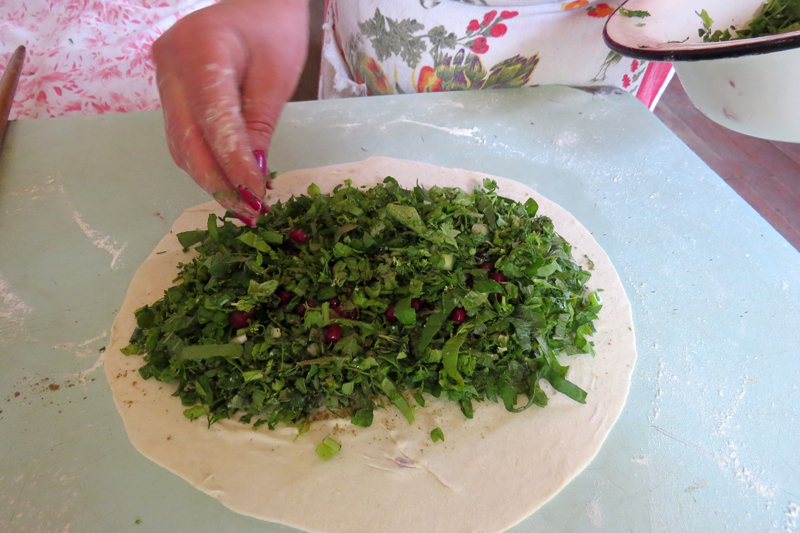 Закладывает начинку - разные сорта мелко нарезанной зелени, зёрнышки граната.